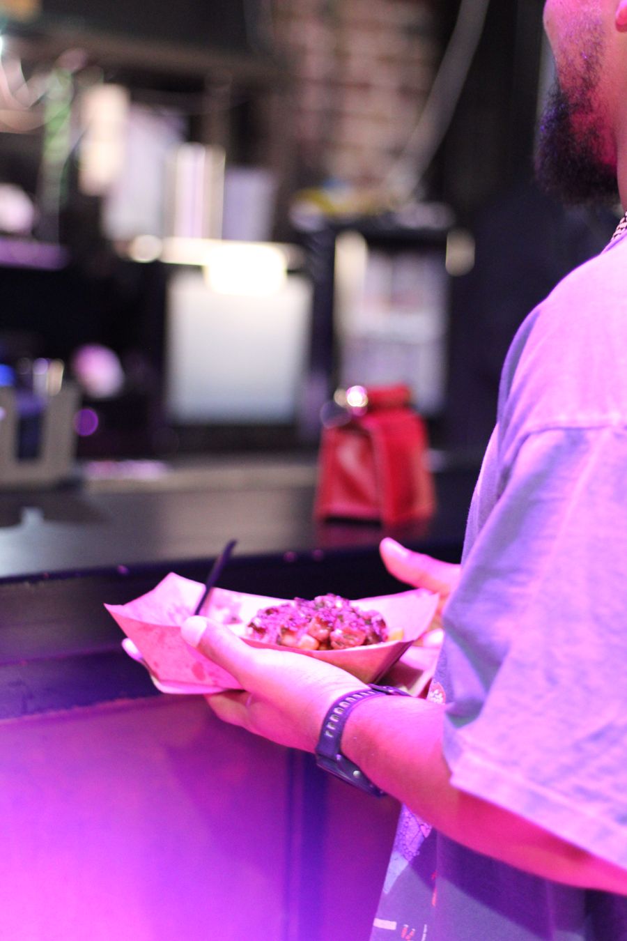 Guest holding a plate of steak and chips under pink lights